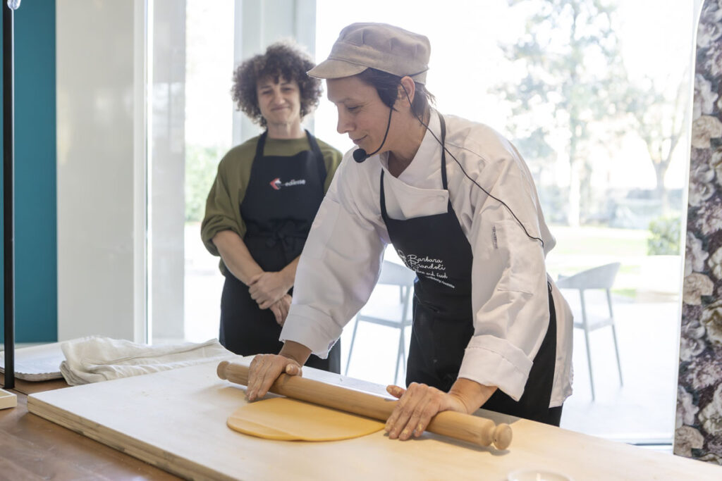 An Emilian pasta maker rolls out fresh pasta with a rolling pin during a culinary team-building event
